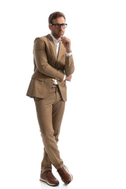 Yakışıklı iş adamı bacak bacak üstüne atıyor, kolunu tutuyor ve beyaz arka planda gözlük takıyor.