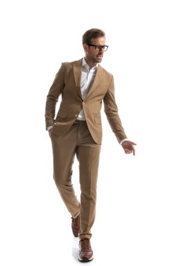 Yakışıklı bir adam kameraya doğru yürüyor, bir elini cebinde tutuyor ve yan tarafa bakıyor. 