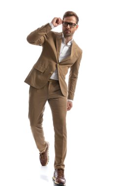 Yakışıklı genç adam beyaz arka planda yürürken gözlüklerini düzeltiyor.