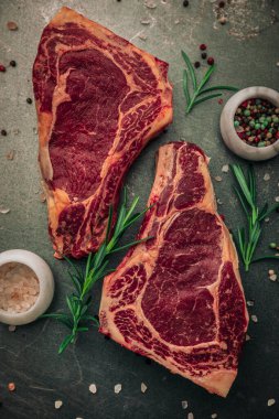 İki parça kırmızı et, tuz ve biber kâseleri ve etrafa biraz serpiştirilmiş biberiye ve demir masanın üstüne biberiye.