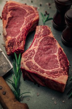 Demir masa üzerinde iki parça kırmızı et üzerine tuz ve biber serpiştirilmiş biberiye ve satır bıçağı ve tuz ve biber öğütücüleri.