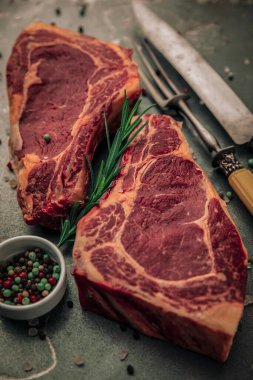 Demir tahtanın üzerinde pişmemiş iki parça bifteğin estetik resmi biberiyeli küçük bir kase biber, biraz tuz, biber ve çatal bıçak serpiştirme. 