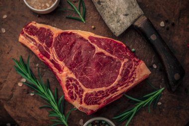 Kırmızı bifteğin üst görüntüsü, otlar, pembe tuz kaseleri ve ahşap kesme tahtasının tepesinde büyük bir bıçakla renkli biber, yiyecek konsepti.