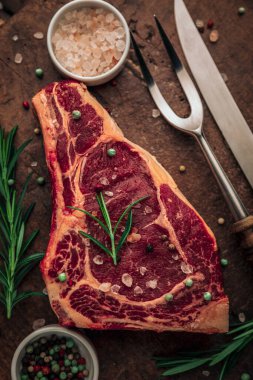 Pişmemiş kırmızı et, yeşil otlar ve tuz ve biber parçacıkları ahşap doğrama tahtasının tepesinde kap ve kaselerin yanında.