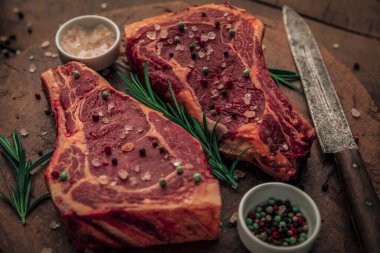 Eski kırsal kesim tahtasının tepesine bıçak, kase dolusu tuz ve biber serpiştirilmiş pişmemiş biftek ve otlar serpiştirilebilir. 