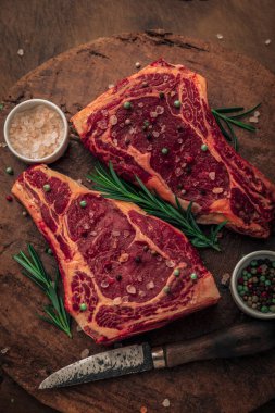 Üzerinde tuz ve biber serpintileri olan iki parça kırmızı etin üst görüntüsü ve ahşap doğrama tahtasının tepesinde pembe tuz, renkli biber ve bıçakla biberiye.