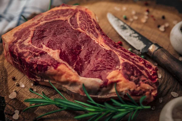 Pişmemiş kırmızı et, biberiye, bıçak, tuz ve biber konsepti eski kırsal kesim tahtasının üstünde. 