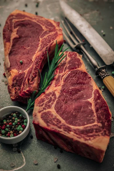 Demir tahtanın üzerinde pişmemiş iki parça bifteğin estetik resmi biberiyeli küçük bir kase biber, biraz tuz, biber ve çatal bıçak serpiştirme. 
