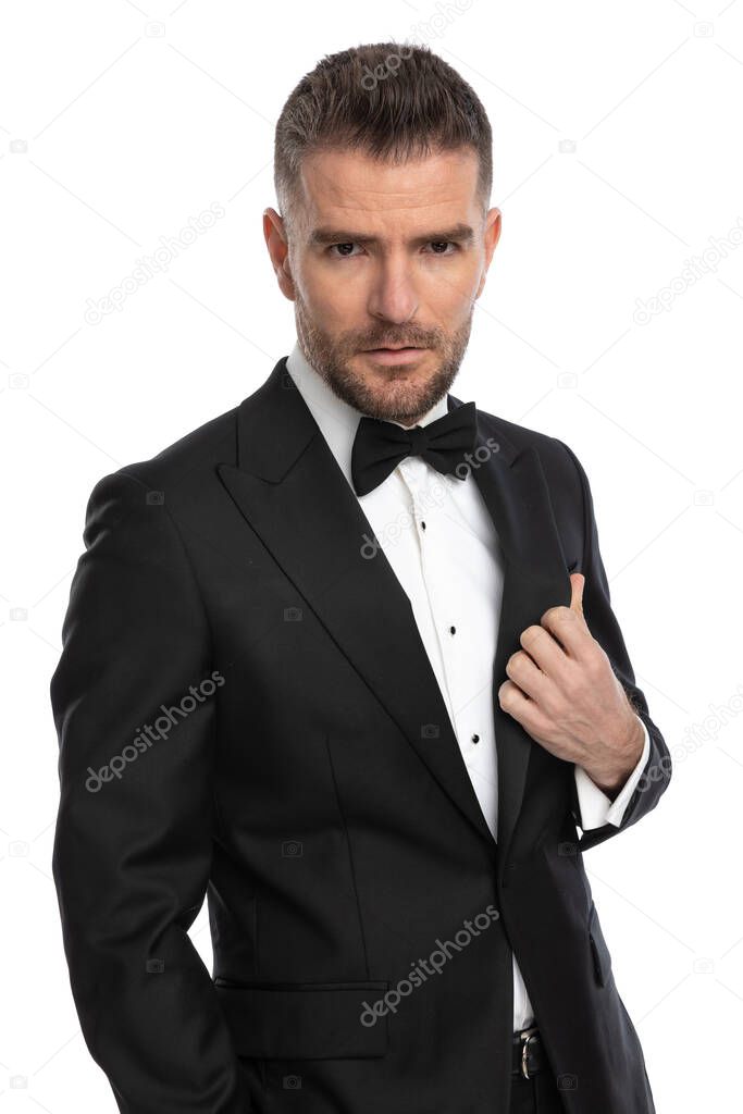portrait of a cool businessman arranging his tux and looking at the camera with a deep look 