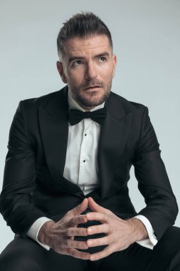 Oturmuş iş adamı gözlerini kaçırıyor, ellerini birarada tutuyor ve havalı bir tavırla poz veriyor.