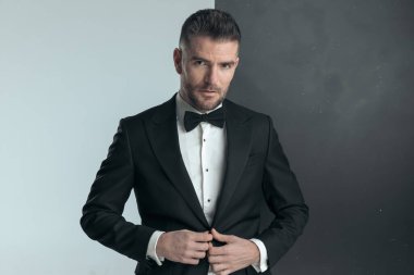 Yakışıklı manken ceketini kapatıyor ve parmakları düğmede poz veriyor. 