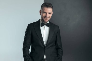 Smokinli zarif iş adamı kameraya gülümsüyor ve elleri cebinde poz veriyor.