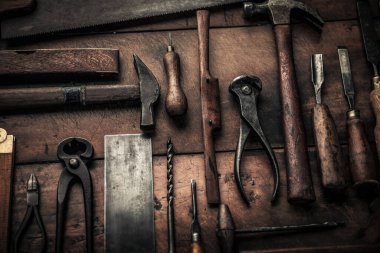 close up picture of rusty old carpentry tools of wooden workbench, hammer, pincers, drill, square 