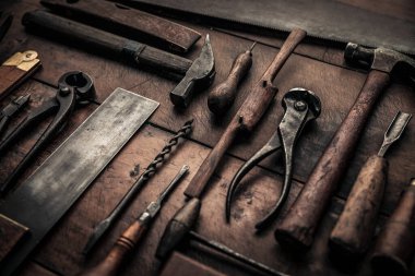 close up picture of rusty pinces, hammer, drilles, screwdriver, spokeshave and others on wooden working table 