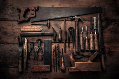 table top view of carpenter workbench full of old rusty tools including hammer, chisel, pincers, drills, gouges and others  