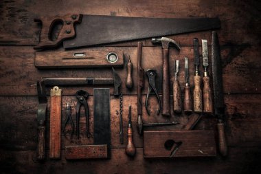 craftsmanship concept illustrated by collection of old carpentry tools on wooden workbench with chisel, spirit level, pincers, handsaw, screwdriver 