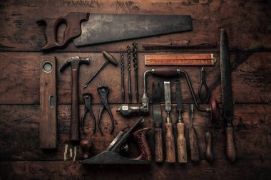 workbench full of rusty old carpenter tools for a craftsmanship concept, pinces, crowbar, gouge, planer, ruler, hammer, chisel, rabone, spirit level in a close up view