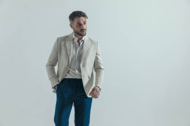 Tıraşsız seksi bir adam. Gömleği bağlı değil. El ele tutuşmuş. Stüdyoda gri arka planda yürümeye çalışıyor.