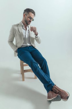 confident man in suit holding hand in pocket and looking to side while posing in a fashion way on grey background in studio