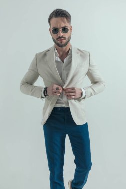 Yakası açık ceketli, ceketli ve stüdyoda gri arka planda yürüyen çekici bir genç.