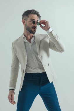 Takım elbiseli, yakalı, güneş gözlüğü takan ve tamir eden havalı bir iş adamı. Stüdyoda gri arka planda havalı poz veriyor.