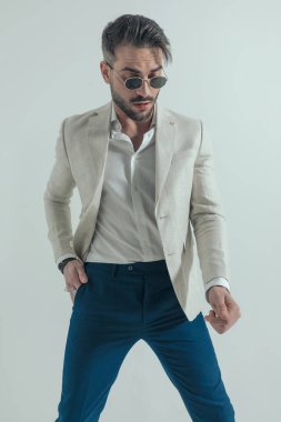 Bağlı olmayan, güneş gözlüklü, el ele tutuşan ve gri arka planda havalı bir tavırla aşağıya bakan seksi adam. 