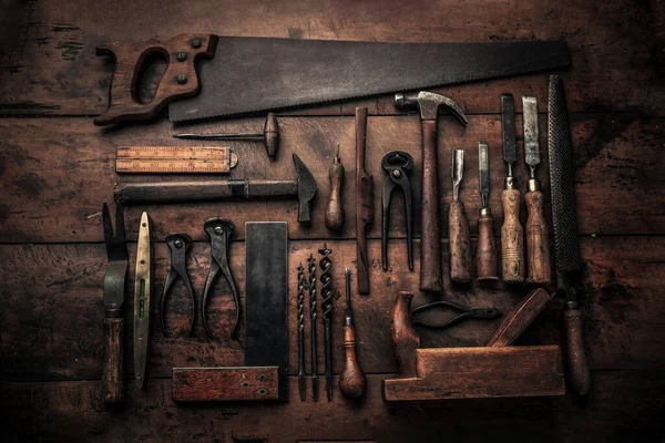 Çekiç, keski, kıskaç, matkaplar, oyuklar ve diğerleri gibi eski paslı aletlerle dolu marangoz tezgahının üst görüntüsü  