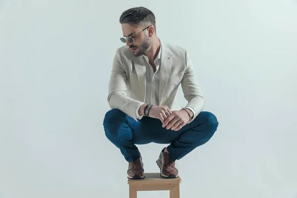 Attractive Crouched Man Sunglasses Touching Palms Looking Side Grey Background — Foto de Stock