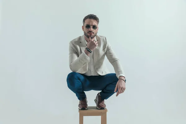 Thoughtful Businessman Glasses Holding Hand Chin Crouching Wooden Chair Front — Fotografia de Stock