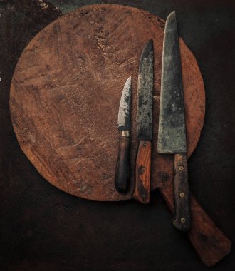 Pişirme konsepti, eski ahşap kesme tahtasının tepesinde, paslı metalik zemin üzerinde üç karbon çelik bıçak setiyle gösterilmiştir.