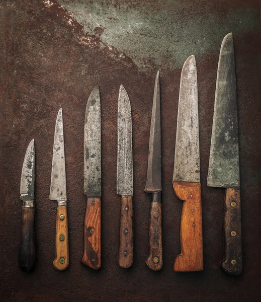 flat lay of various carbon steel knives with wooden handle on old rusty metallic background