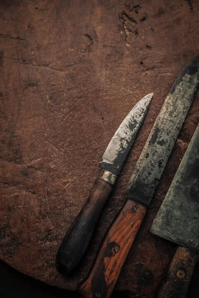 close up of small utility knives and kitchen knife with carbon steel blade on top of rustic old chopping board