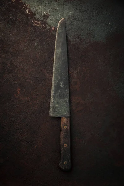 vintage carbon steel kitchen knife with wooden handle on top of rusty metallic background, table top