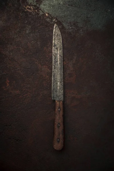top view of carbon steel blade knife with wooden handle on top of rusty metallic background
