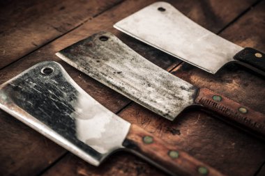 close up picture of three rusty meat butchers with wooden handle on top of tabl