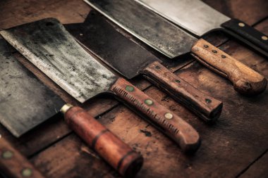 old kitchen collection of different types of meat butchers with sharp blade and wooden handle on top of wooden table 