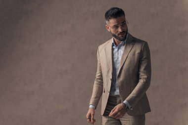 portrait of handsome businessman looking to side and holding arms in fashion pose in front of beige background in studio