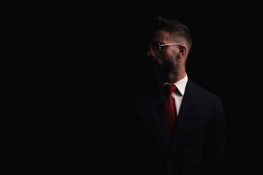 Gözlüklü gizemli bir gencin portresi. Stüdyoda siyah arka plan önünde moda ışığında poz veriyor.