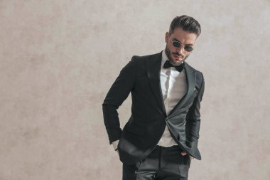 Siyah smokinli zarif bir adamın portresi. Elleri ceplerinde. Stüdyoda bej arka planda poz veriyor.