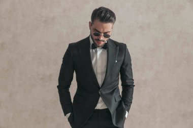 Stüdyoda bej arka planda poz veren, elleri ceplerinde şık şık bir adamın portresi.