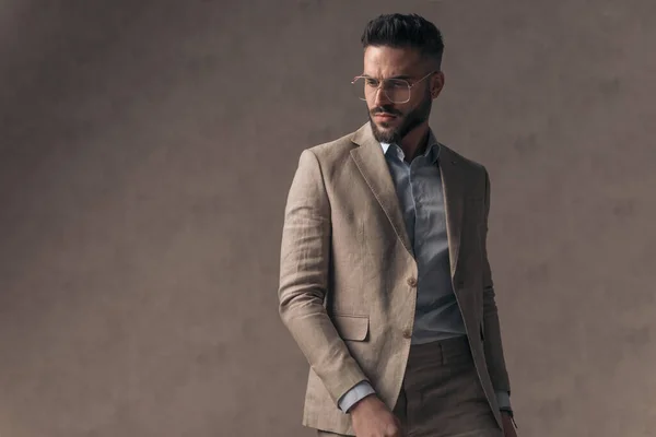 stylish elegant businessman with open collar shirt looking to side and walking in front of beige background in studio