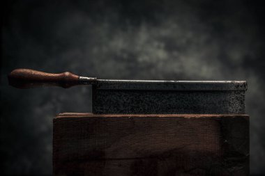 old rusty handsaw with serrated blade in top of wooden workbench in front of dark texture background