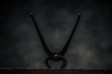 carpentry concept illustrated by rusty pincer on top of wooden work in front of dark texture background 