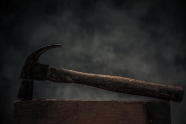 picture of old vintage rusty hammer for carpentry on top of workbench for concept of carpentry in dark texture background 