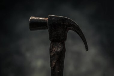 vintage rusty hammer for carpentry and woodwork in front of dark texture background 