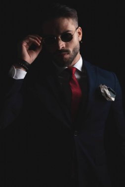 cut out picture of elegant guy in suit with red tie and handkerchief adjusting retro sunglasses in studio