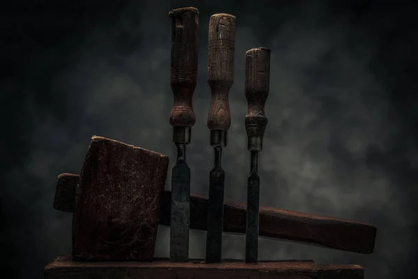 collection of old rusty carbon steel chisels with carving hammer behind in front of dark texture background in studio