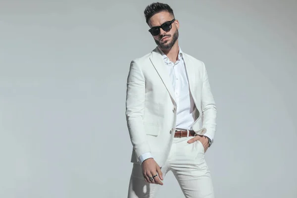 smart casual guy in white suit with open collar shirt holding hand in pocket and confidently posing on grey background