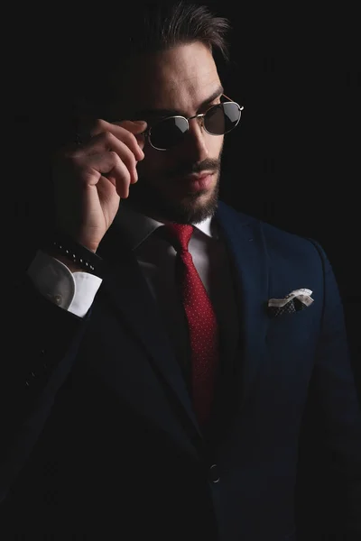 cut out picture of attractive stylish man adjusting retro sunglasses, wearing navy blue elegant suit with red tie and handkerchief and posing