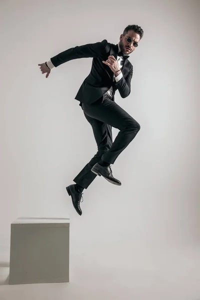 dynamic man wearing tuxedo illustrating concept of new life, leaving old things behind and embracing change on grey background